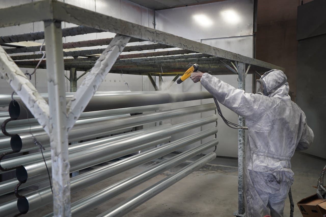 Operator powder coating long metal tubes in a spray booth